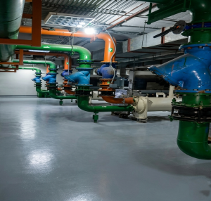 A clean, brightly lit modern industrial HVAC plant room with an array of polished green, orange, and blue pipes.